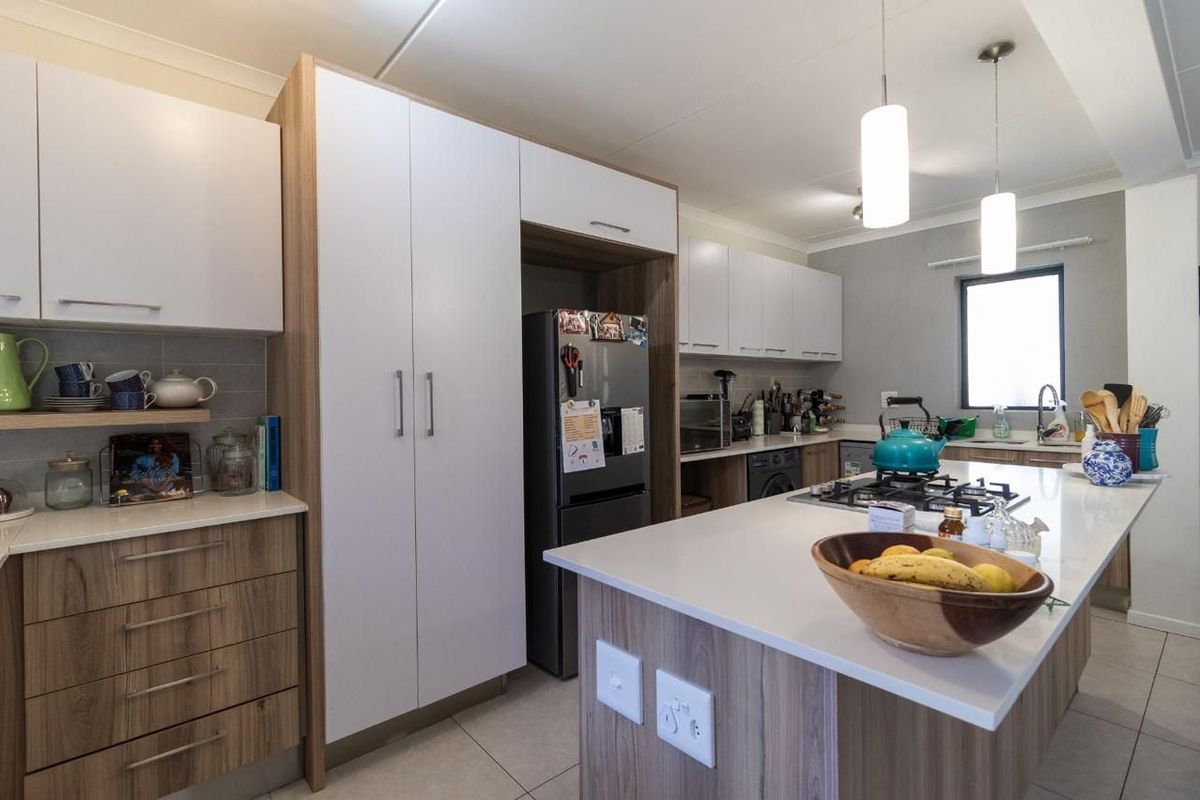 Modern kitchen featuring a central island with a gas hob, ample built-in cabinetry, stone countertops, and contemporary pendant lighting.