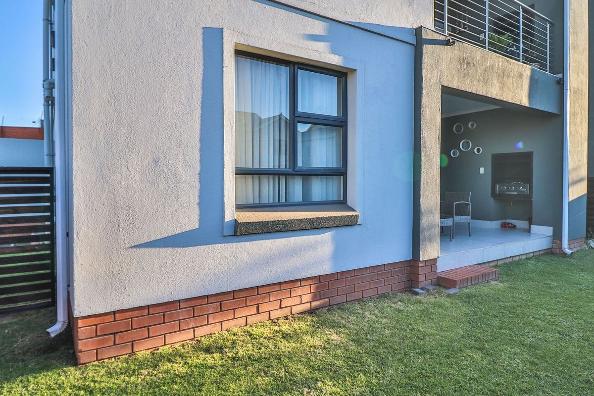 Rear exterior view of the apartment featuring a covered patio with a built-in braai, brick base detailing, and a balcony above.