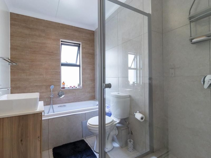 Modern bathroom featuring a built-in bathtub, separate glass-enclosed shower, vanity basin, and neutral tiled finishes throughout.