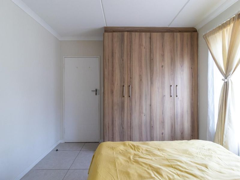 A well-maintained bedroom featuring neutral tiled flooring, a coved ceiling, and a large wood-finish built-in wardrobe.