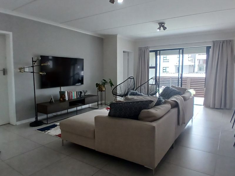 A bright and spacious living room featuring large format floor tiles, neutral wall tones, and direct access to a private balcony through sliding glass doors.