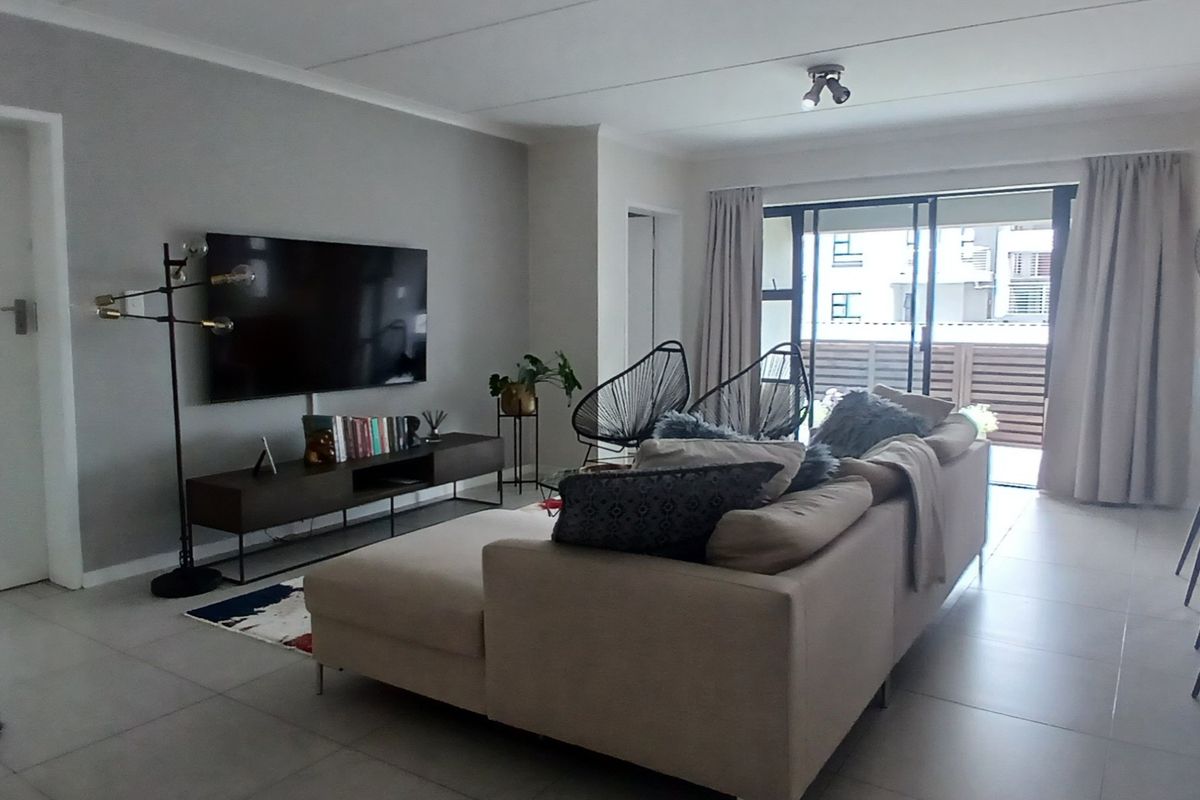 A bright and spacious living room featuring large format floor tiles, neutral wall tones, and direct access to a private balcony through sliding glass doors.