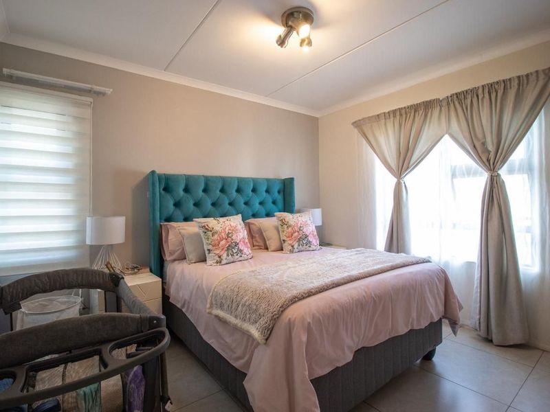 A well-maintained bedroom featuring neutral wall tones, tiled flooring, and dual window treatments including roller blinds and curtains.