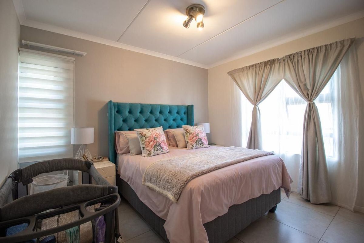 A well-maintained bedroom featuring neutral wall tones, tiled flooring, and dual window treatments including roller blinds and curtains.