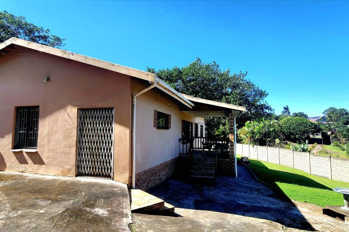 Rear view of the house featuring a concrete patio, security gates, and a large garden area enclosed by a perimeter wall.