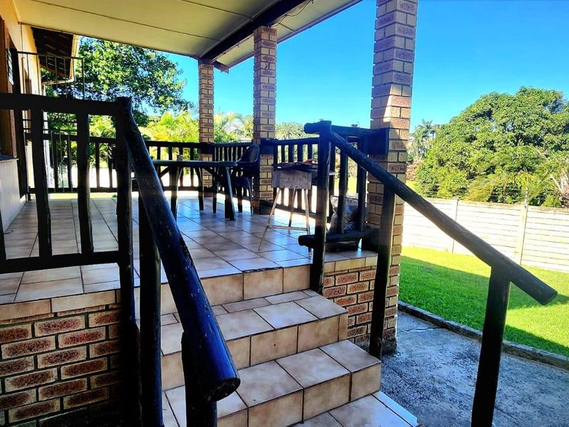A covered outdoor patio featuring tiled flooring, brick support pillars, and a timber balustrade, overlooking a private garden area.