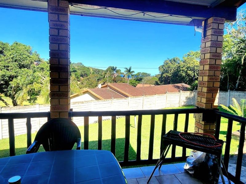 A covered patio area featuring brick pillars and a timber balustrade, overlooking a garden and surrounding residential landscape.