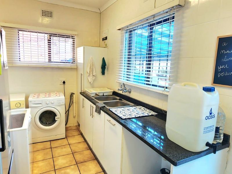 A functional laundry room featuring built-in cabinetry, a double basin sink, tiled flooring, and space for laundry appliances.