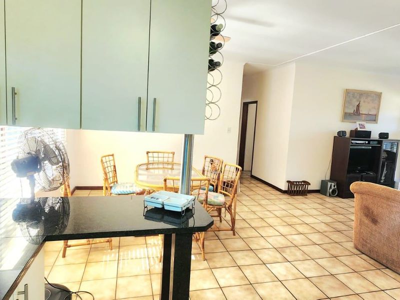 Open plan living area featuring a kitchen with granite countertops and breakfast bar, flowing into a dining and lounge space with tiled flooring.