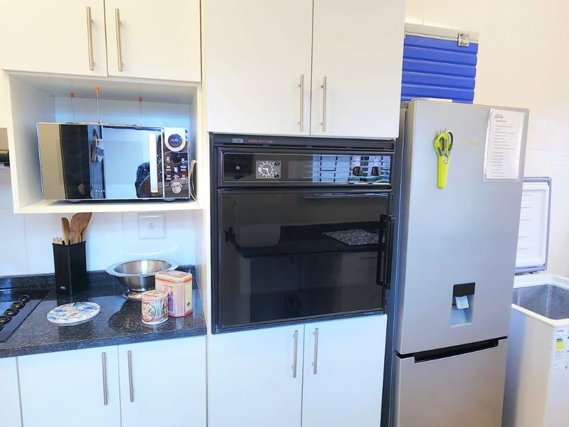 A functional kitchen featuring white cabinetry, dark granite countertops, a built-in oven, and an electric hob with an extractor fan.