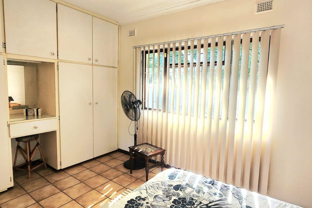 A bedroom featuring built-in cupboards with an integrated vanity, tiled flooring, and vertical blinds covering the window.