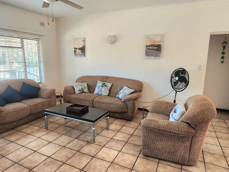 A functional living room featuring tiled flooring, a ceiling fan, and large windows with venetian blinds, offering a neutral base for updates.