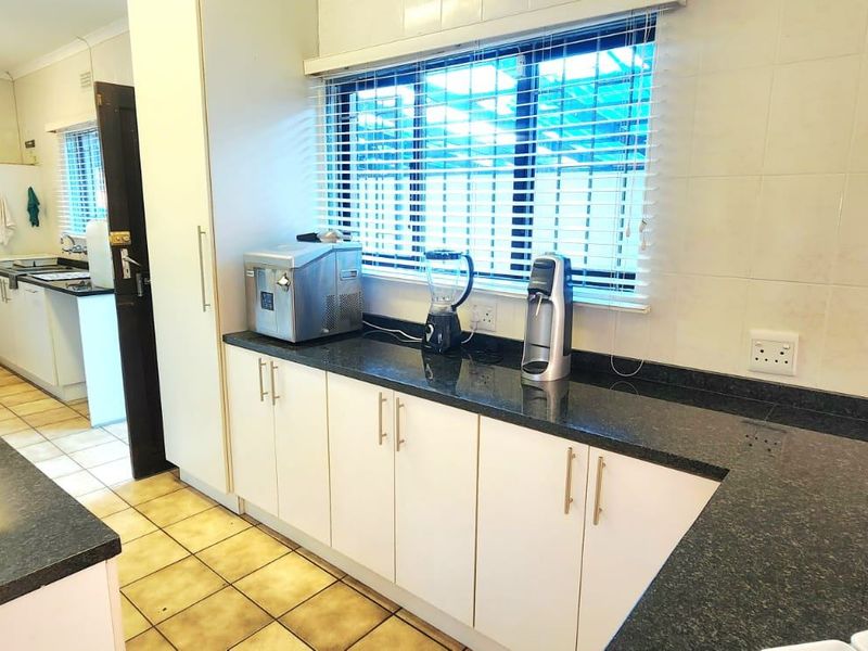 Functional kitchen featuring granite countertops, ample built-in cabinetry, and tiled flooring, with an adjacent scullery area visible through the doorway.