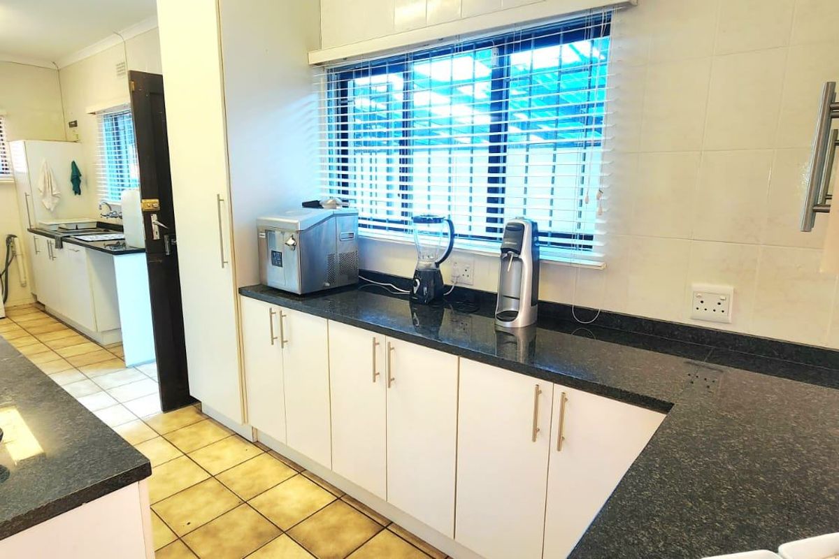 Functional kitchen featuring granite countertops, ample built-in cabinetry, and tiled flooring, with an adjacent scullery area visible through the doorway.