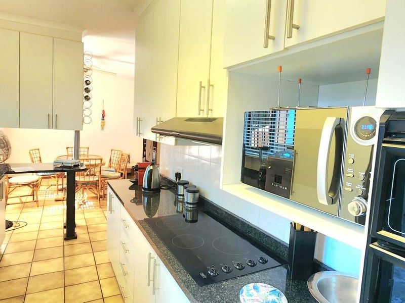 A functional kitchen featuring built-in cabinetry, granite countertops, an integrated electric hob, extractor fan, and built-in oven with microwave.