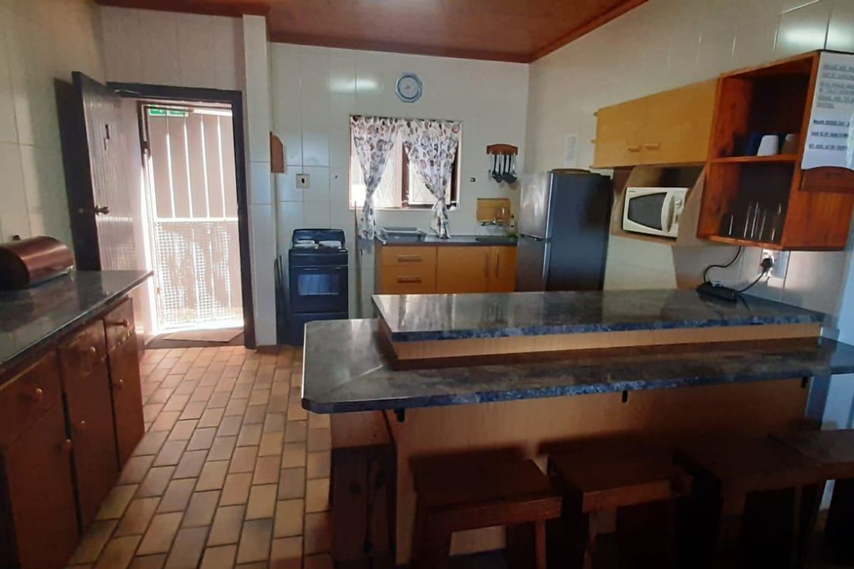 A functional kitchen featuring built-in wooden cabinetry, laminate countertops with an integrated breakfast bar, and tiled flooring with direct access to an exterior door.