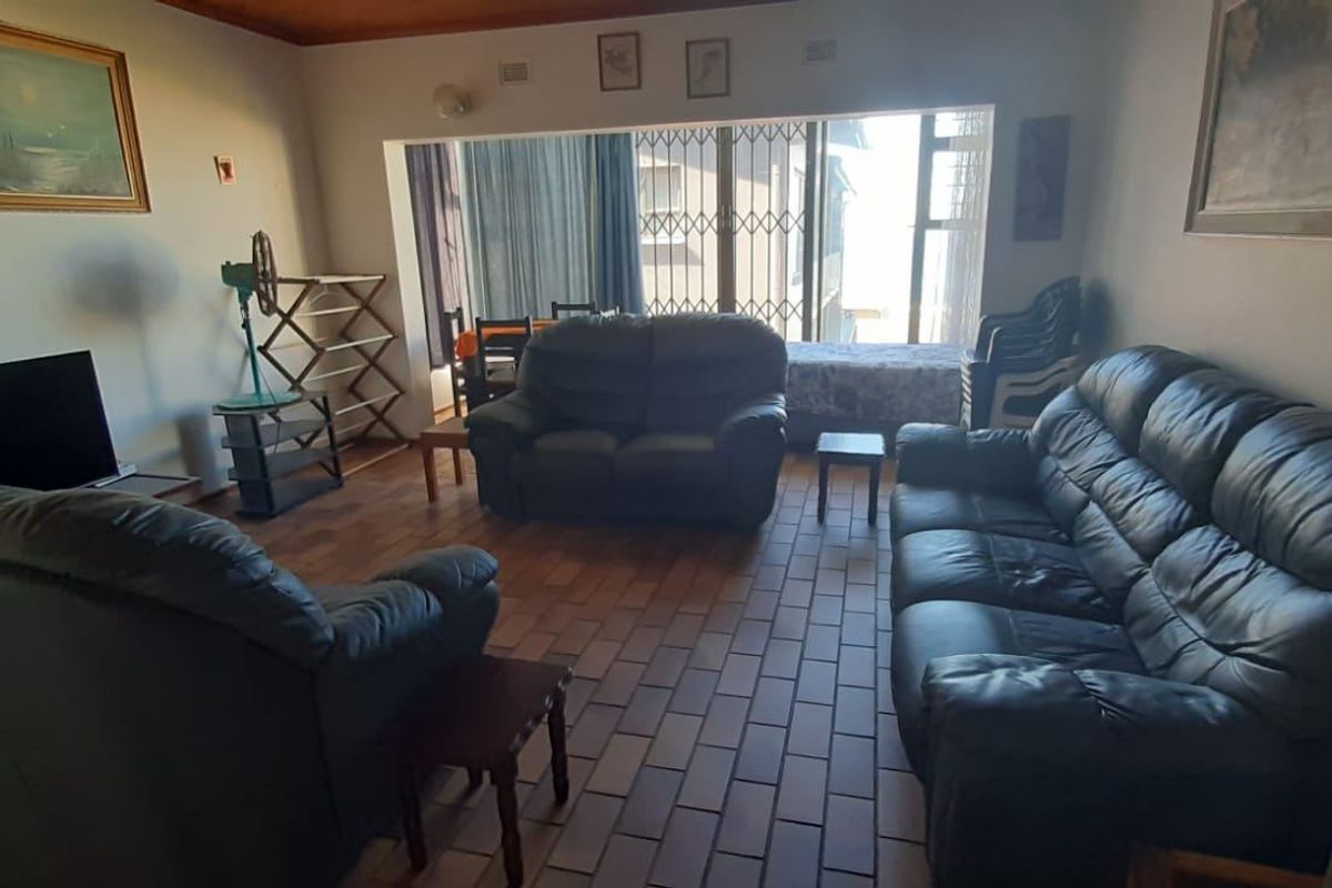 A spacious living room featuring tiled flooring, timber ceiling trim, and large windows with security gates, offering a functional and well-lit living area.
