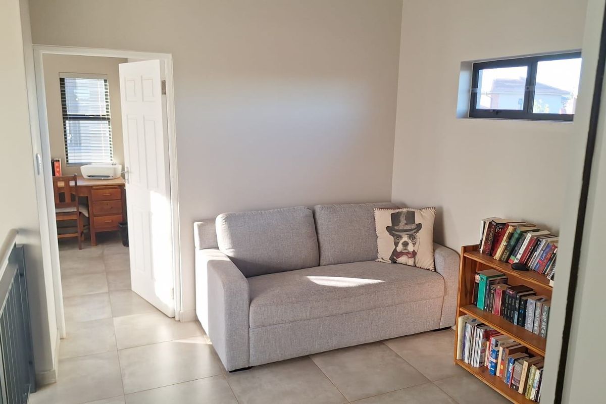 A bright living area featuring neutral tiled flooring, a horizontal window, and access to an adjacent room, suitable for a cozy lounge or study space.