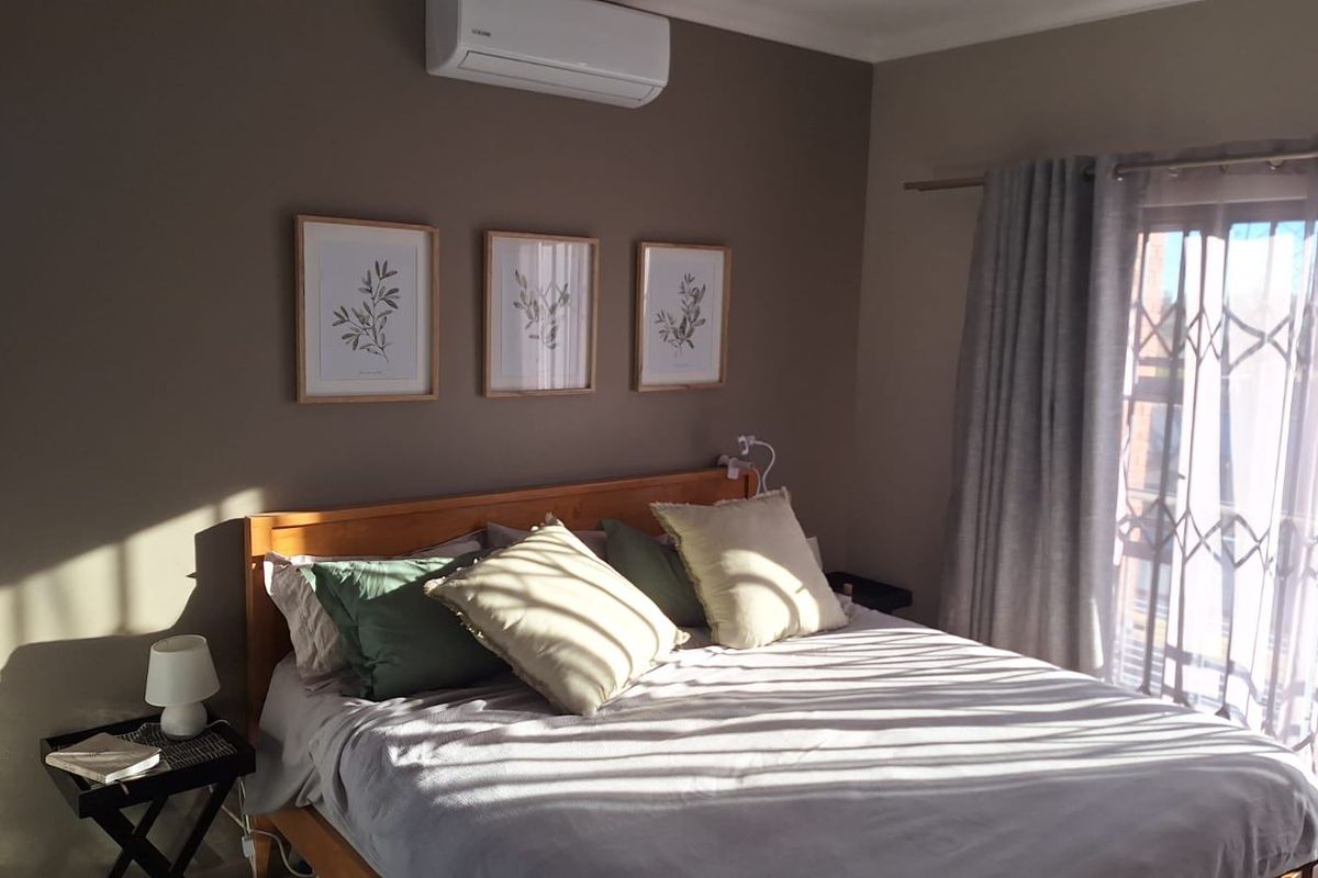 A well-maintained bedroom featuring a wall-mounted split-system air conditioner, security gate on the sliding door, and neutral wall tones.