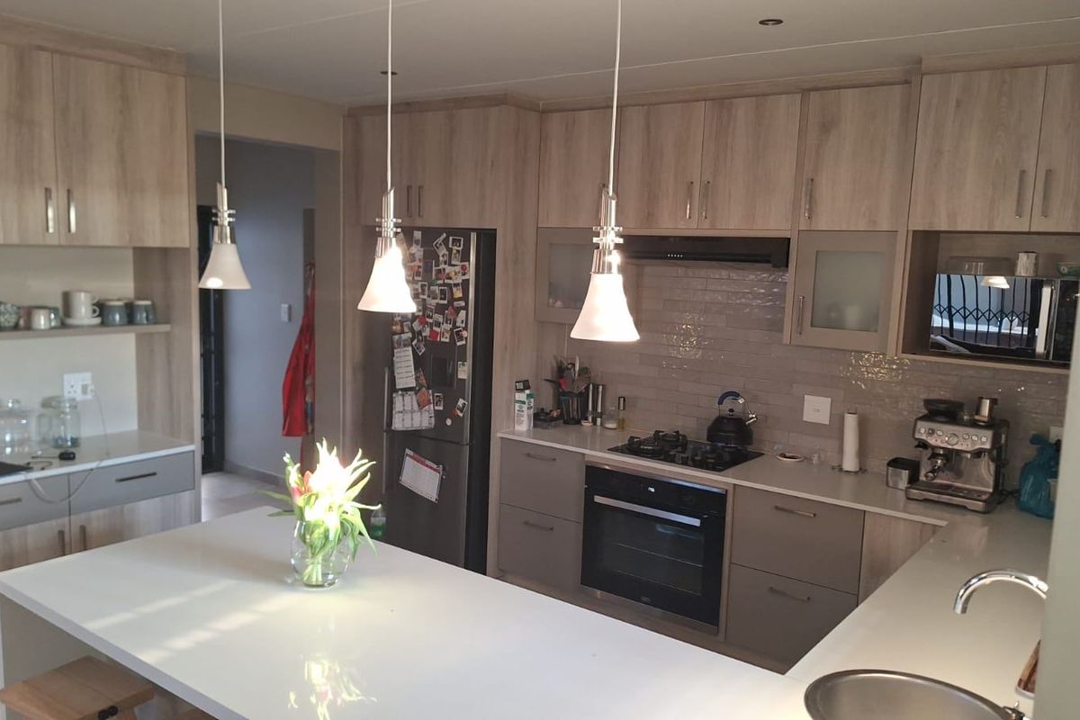 Modern kitchen featuring light wood-tone cabinetry, stone countertops, a central island, and integrated appliances including a gas hob and oven.