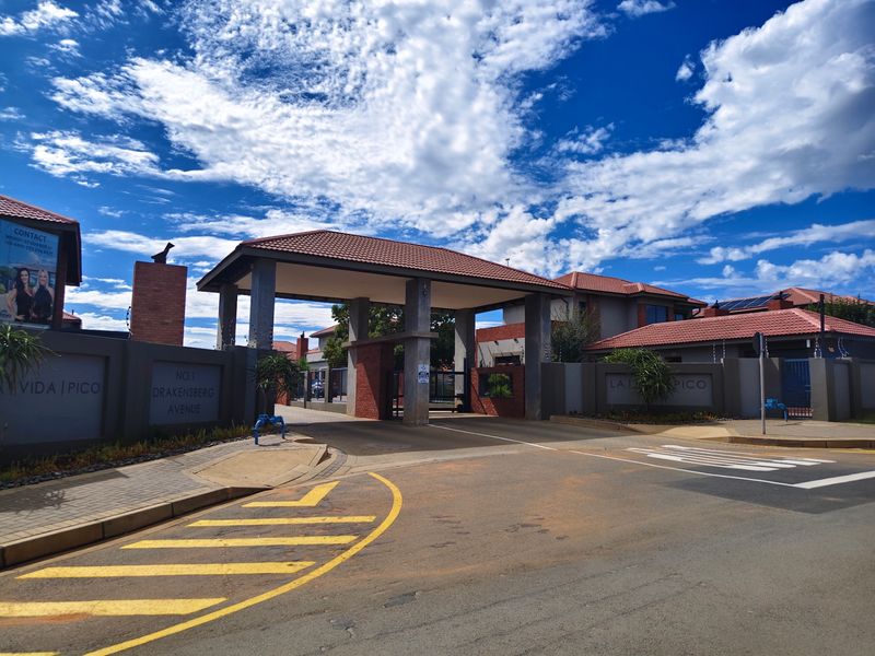 The main entrance to the townhouse complex featuring a secure gated access point, brick boundary walls, and a paved driveway.