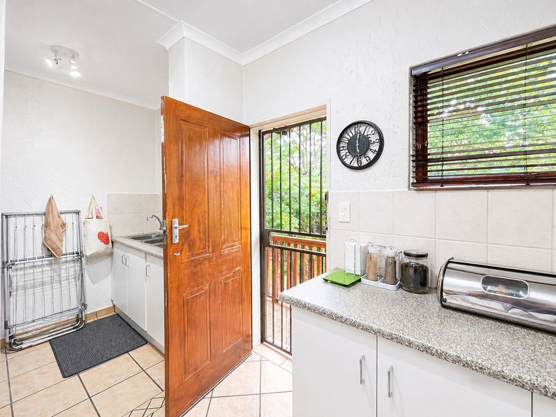 A functional kitchen and laundry area featuring built-in cabinetry, granite-look countertops, a stainless steel sink, and direct access to an outdoor balcony.