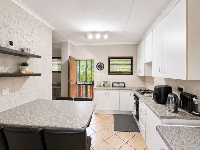 A functional kitchen featuring white cabinetry, granite-look countertops, a built-in gas hob, and tiled flooring, with an adjacent breakfast nook and exterior access.