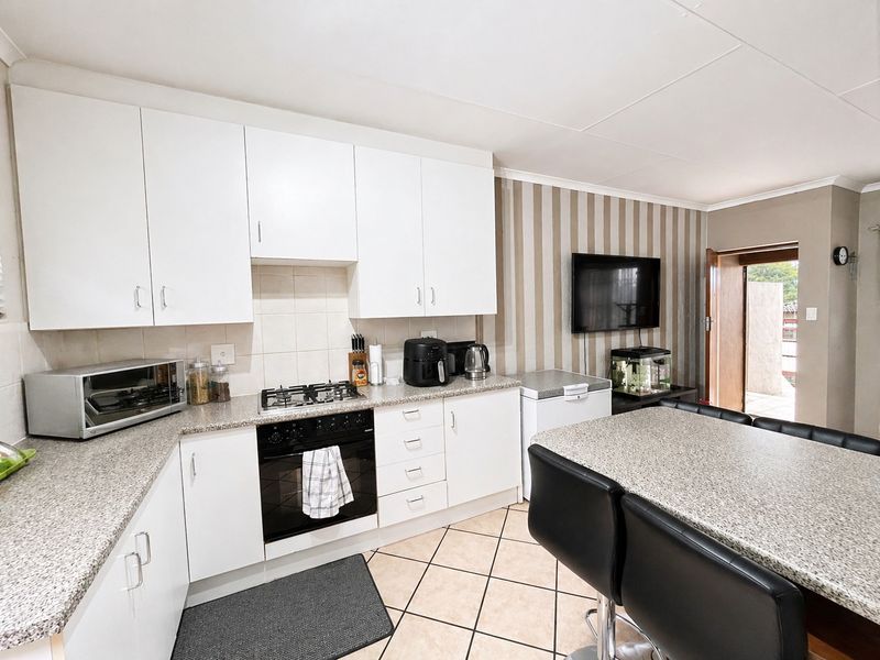 A functional kitchen featuring white cabinetry, granite-look countertops, a built-in oven and gas hob, tiled flooring, and an integrated breakfast bar area.
