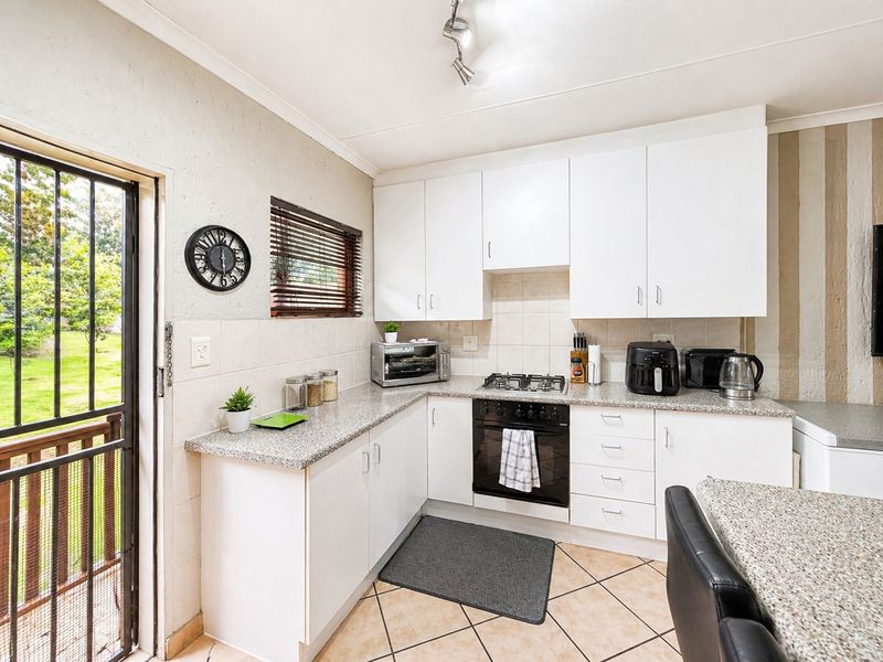 A functional kitchen featuring white cabinetry, granite-style countertops, a built-in oven with gas hob, and tiled flooring with direct access to the outdoors.