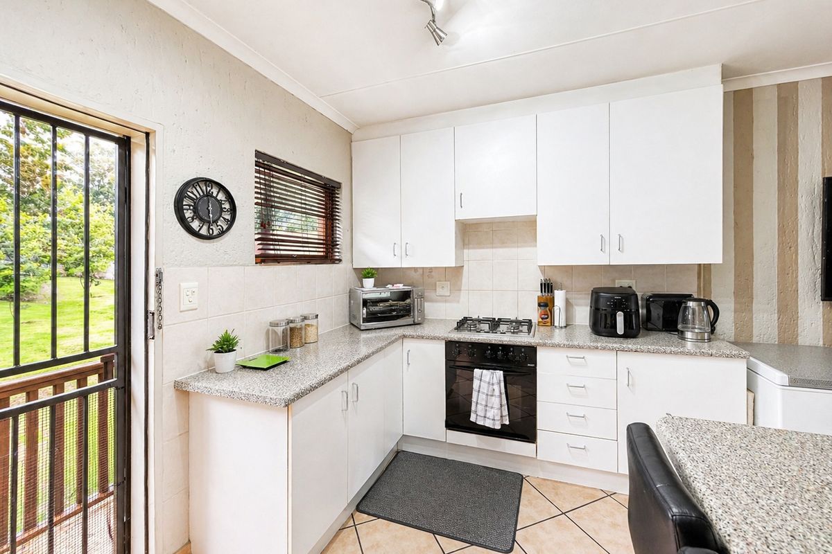 A functional kitchen featuring white cabinetry, granite-style countertops, a built-in oven with gas hob, and tiled flooring with direct access to the outdoors.