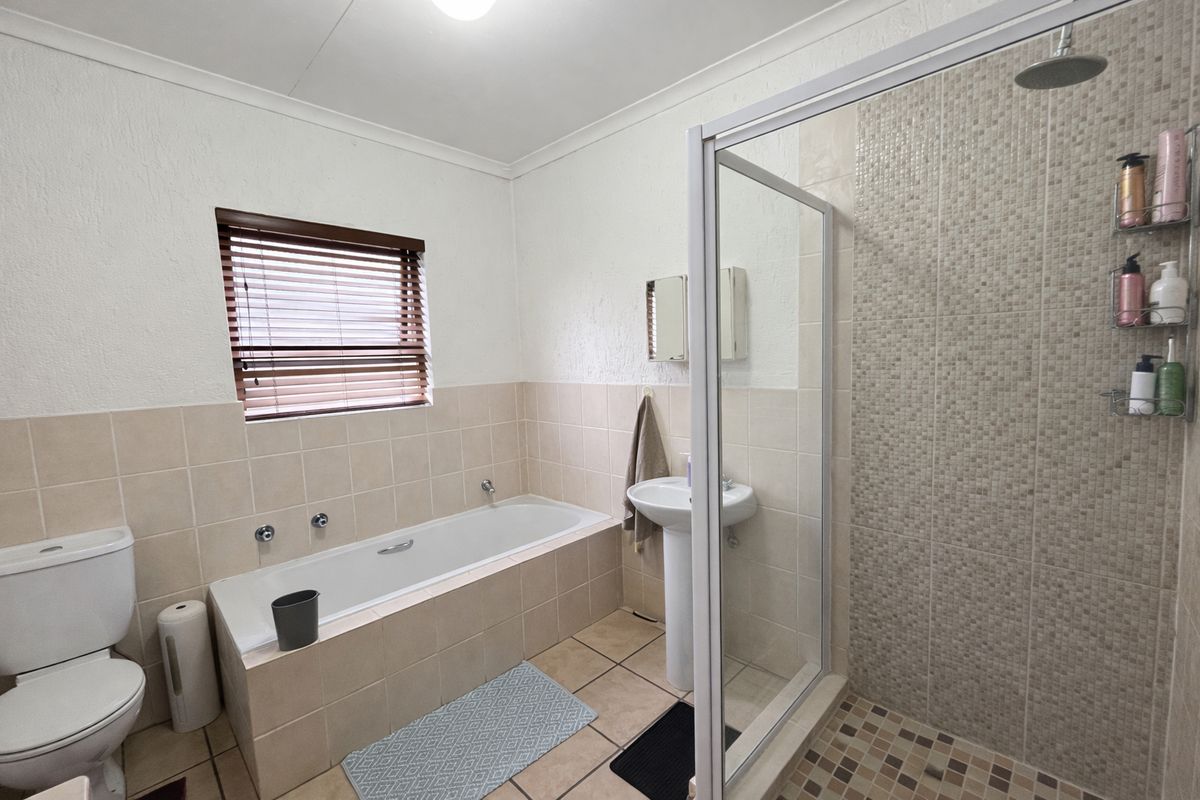 A functional bathroom featuring a built-in bathtub, a separate glass-enclosed shower with mosaic tiling, a pedestal basin, and a toilet.