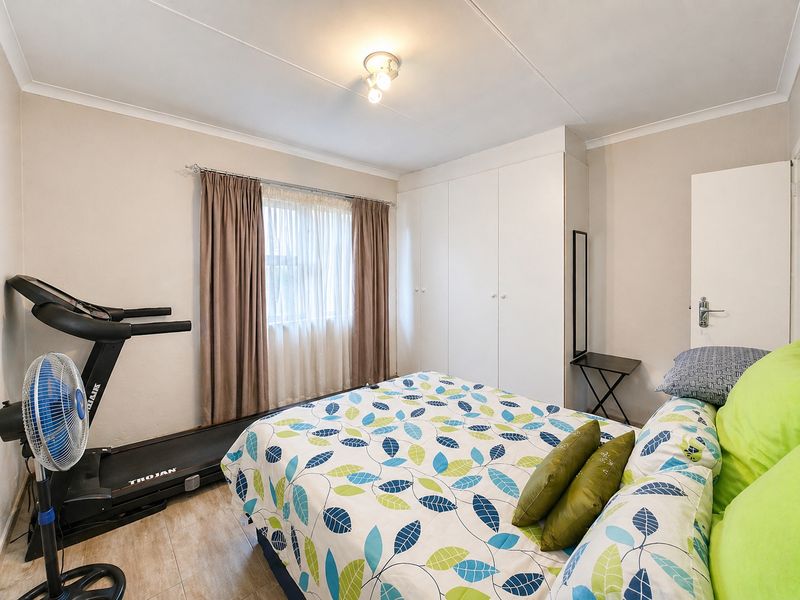 A functional bedroom featuring built-in cupboards, tiled flooring, and a window with curtain tracks, providing a practical and well-lit living space.