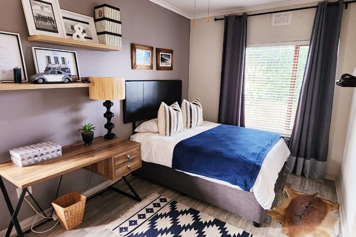 A well-maintained bedroom featuring laminate flooring, floating wall shelves, and venetian blinds, offering a comfortable and functional living space.