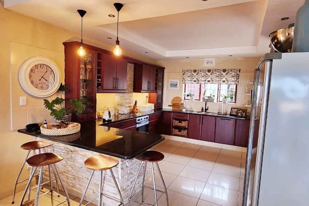 A well-maintained kitchen featuring dark wood cabinetry, granite countertops, a stone-clad breakfast bar, and modern pendant lighting with tiled flooring throughout.