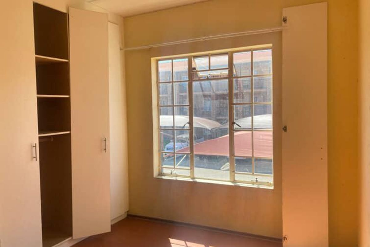 An empty bedroom featuring built-in cupboards and a steel-framed window, offering a functional space ready for personalization.