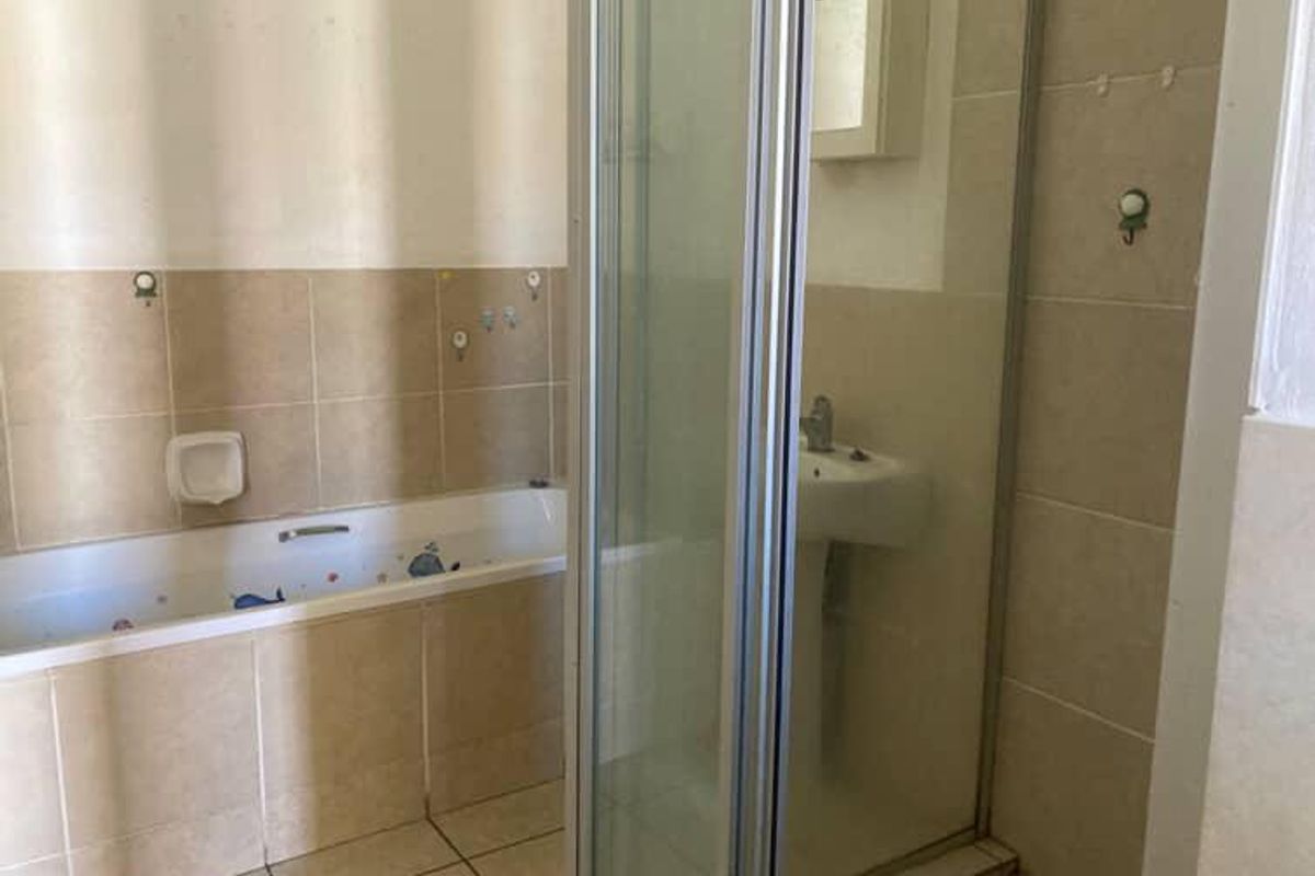 A functional bathroom featuring a bathtub, separate shower enclosure, and pedestal basin with neutral ceramic tiling throughout.