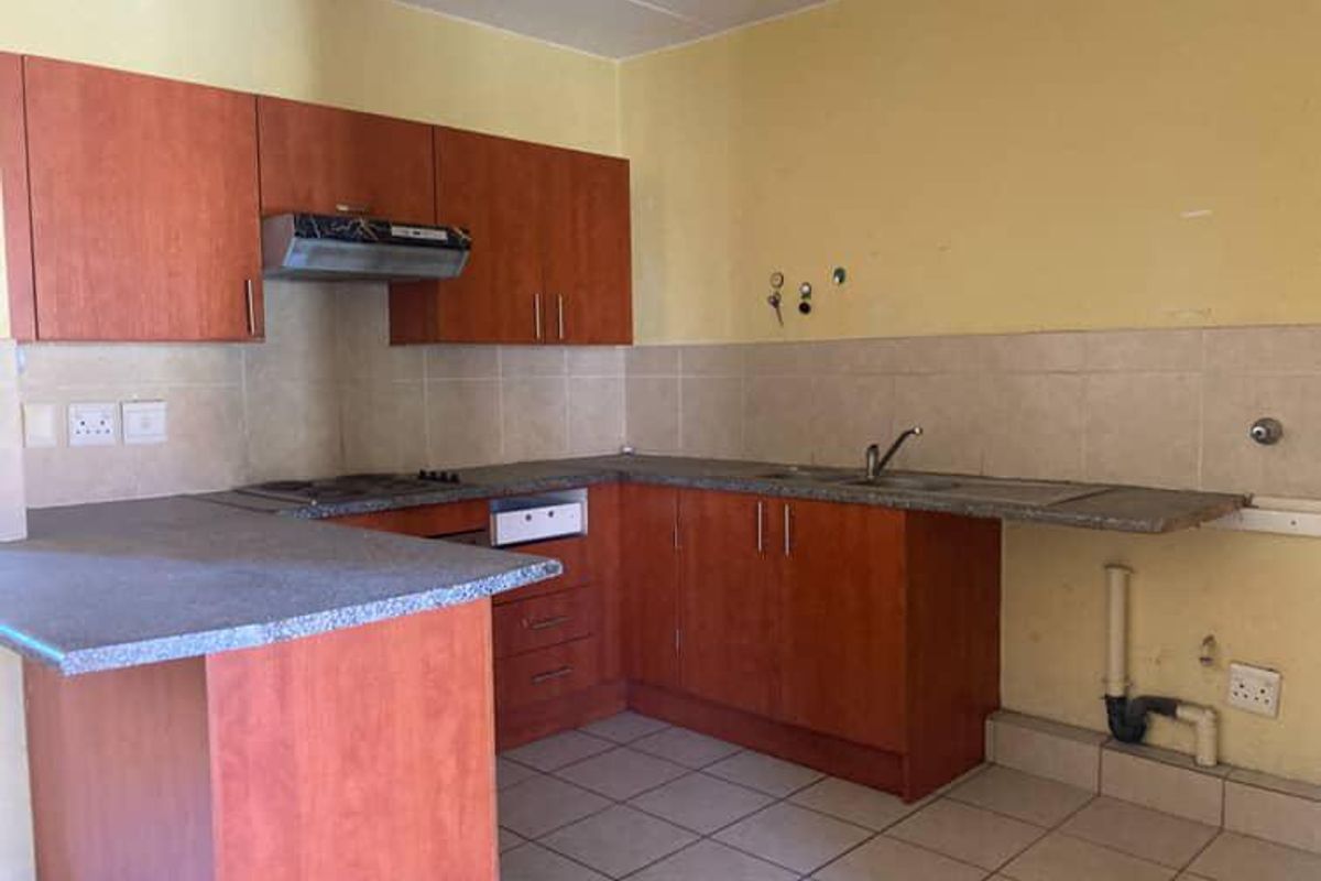 A functional kitchen featuring laminate cabinetry, stone-look countertops, a built-in extractor fan, and tiled flooring, offering a blank canvas for potential renovation.