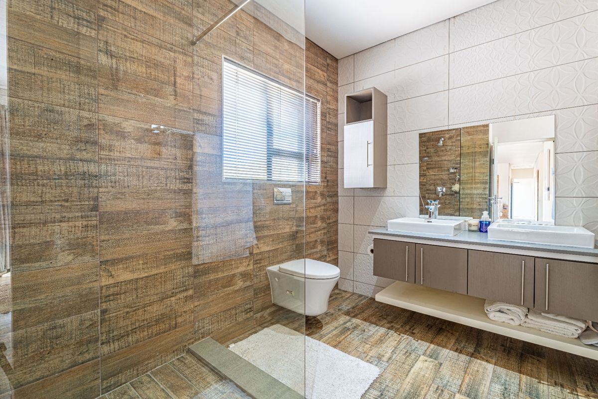 Modern bathroom featuring a wall-mounted toilet, glass shower screen, and a double vanity with integrated sinks and storage cabinetry.