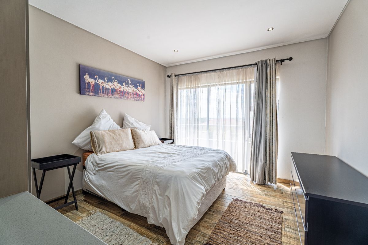 A well-lit bedroom featuring wood-look tiled flooring, recessed ceiling lighting, and a sliding glass door providing access to an outdoor area.