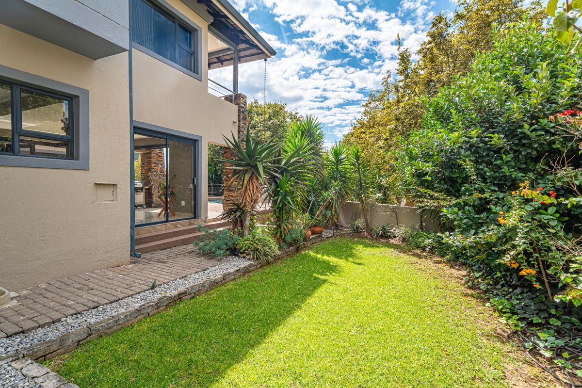 A view of the rear garden featuring a paved walkway, lush lawn, and established landscaping adjacent to the house exterior.