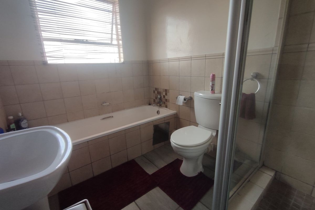 A functional bathroom featuring a bathtub, separate shower enclosure, pedestal basin, and toilet with neutral wall and floor tiling.