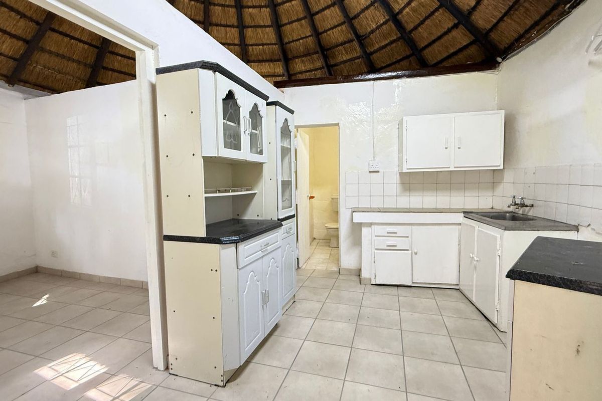 A dated kitchen featuring a unique thatched roof, tiled flooring, and built-in cabinetry, offering significant potential for a modern renovation.