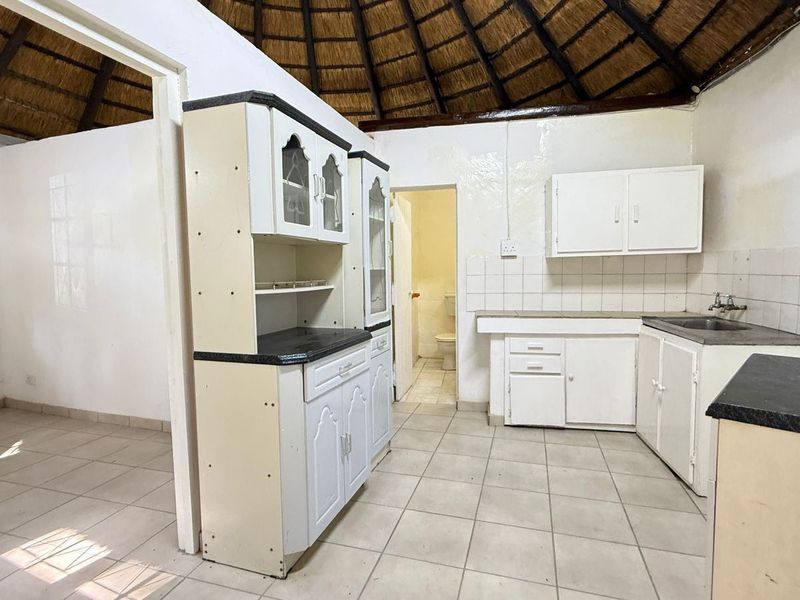 A dated kitchen featuring a unique thatched roof, tiled flooring, and built-in cabinetry, offering significant potential for a modern renovation.