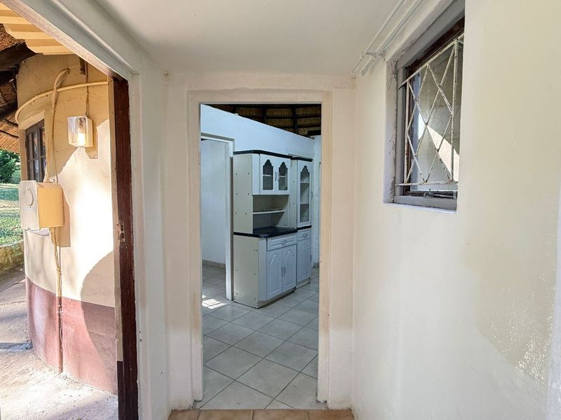 A view through a hallway leading into an adjacent room, featuring tiled flooring and a security-grille window.