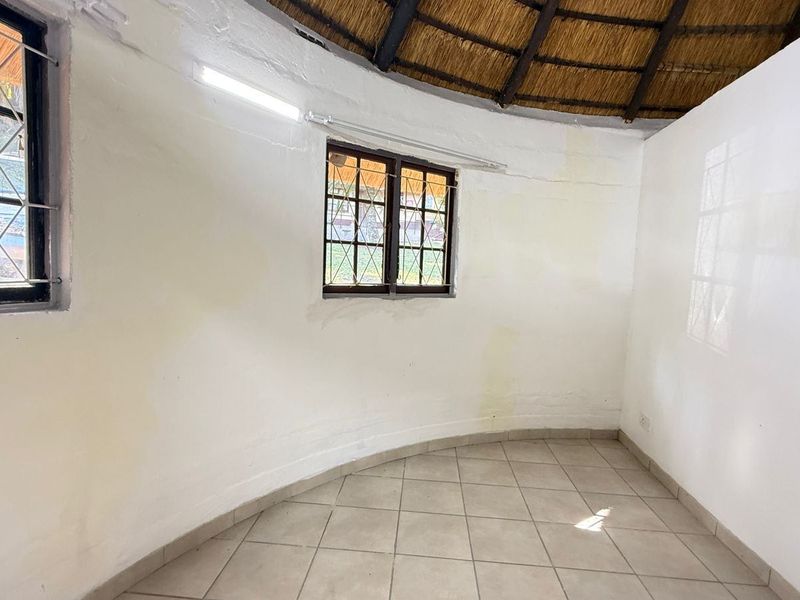 An empty bedroom featuring a unique circular layout, thatched roof ceiling, tiled flooring, and security-barred windows, requiring cosmetic updates to the walls.