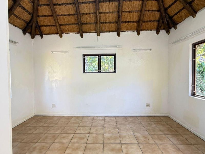 An empty bedroom featuring a traditional thatched roof with exposed timber rafters, ceramic tiled flooring, and security-barred windows.