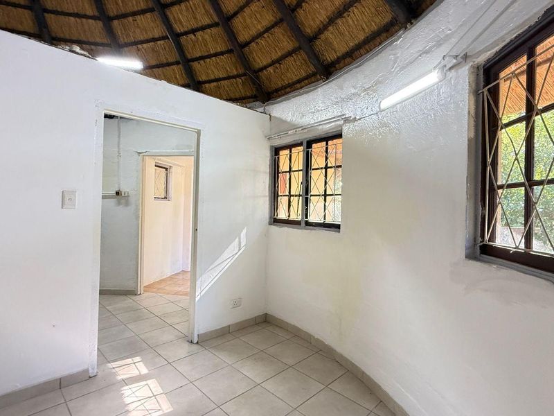 An empty bedroom featuring a traditional thatched roof, tiled flooring, and security bars on the windows, offering a blank canvas for renovation.