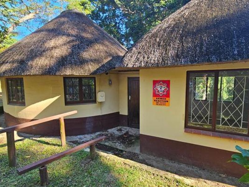 Exterior view of a traditional thatched-roof dwelling featuring security bars on windows and a timber entrance door.