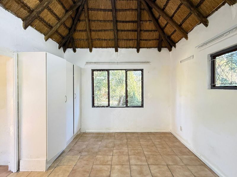 Empty bedroom featuring a traditional thatched roof with exposed rafters, tiled flooring, and built-in storage cupboards.