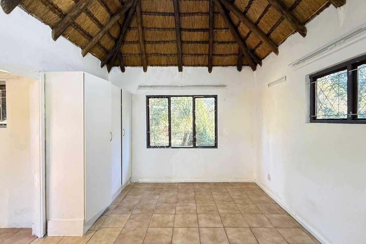 Empty bedroom featuring a traditional thatched roof with exposed rafters, tiled flooring, and built-in storage cupboards.